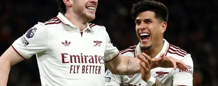 Cúp Community Shield đặt trên sân cỏ Cardiff với cầu thủ Arsenal áo đỏ và Man City áo xanh khởi động dưới ánh đèn sân vận động